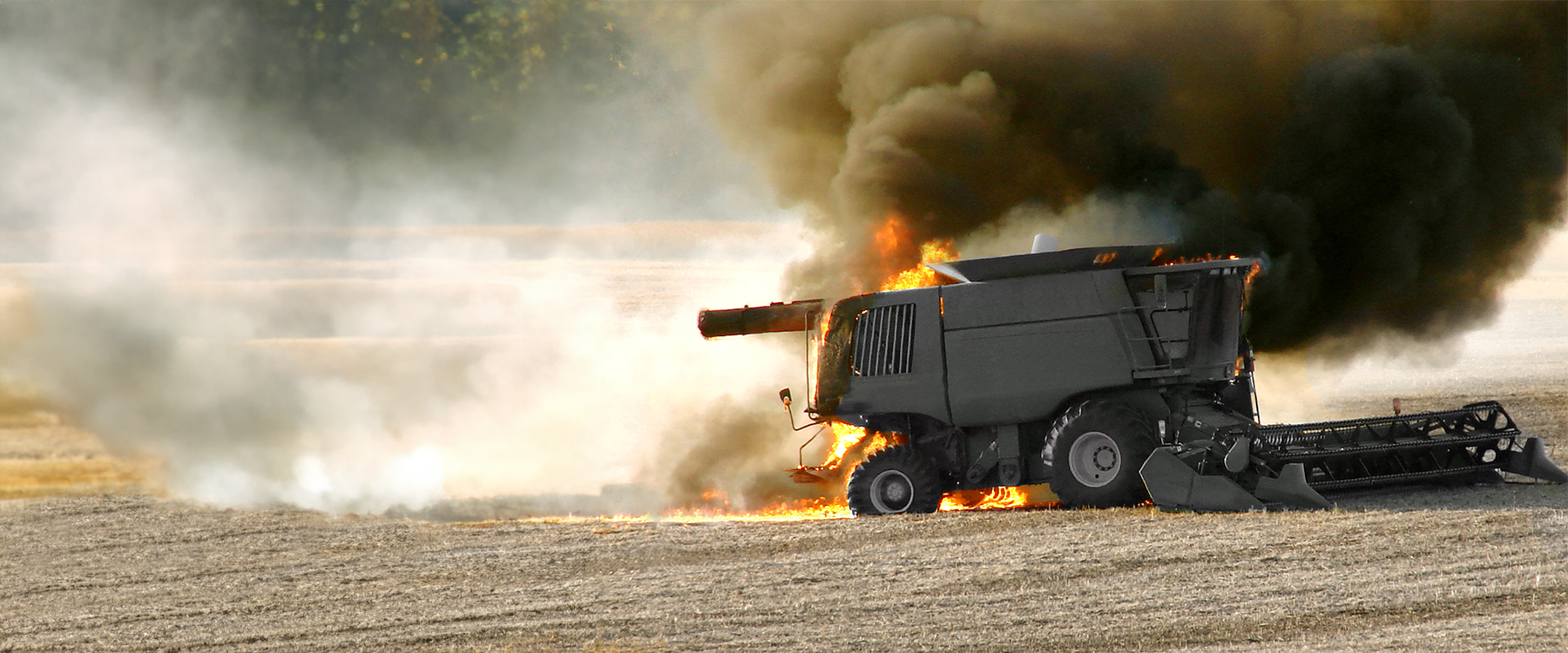 John Deere Combine in a corn field with flames coming out of the back and black smoke rising