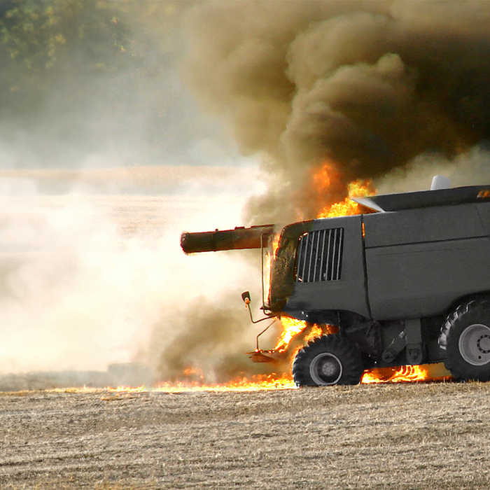 John Deere Combine in a corn field with flames coming out of the back and black smoke rising