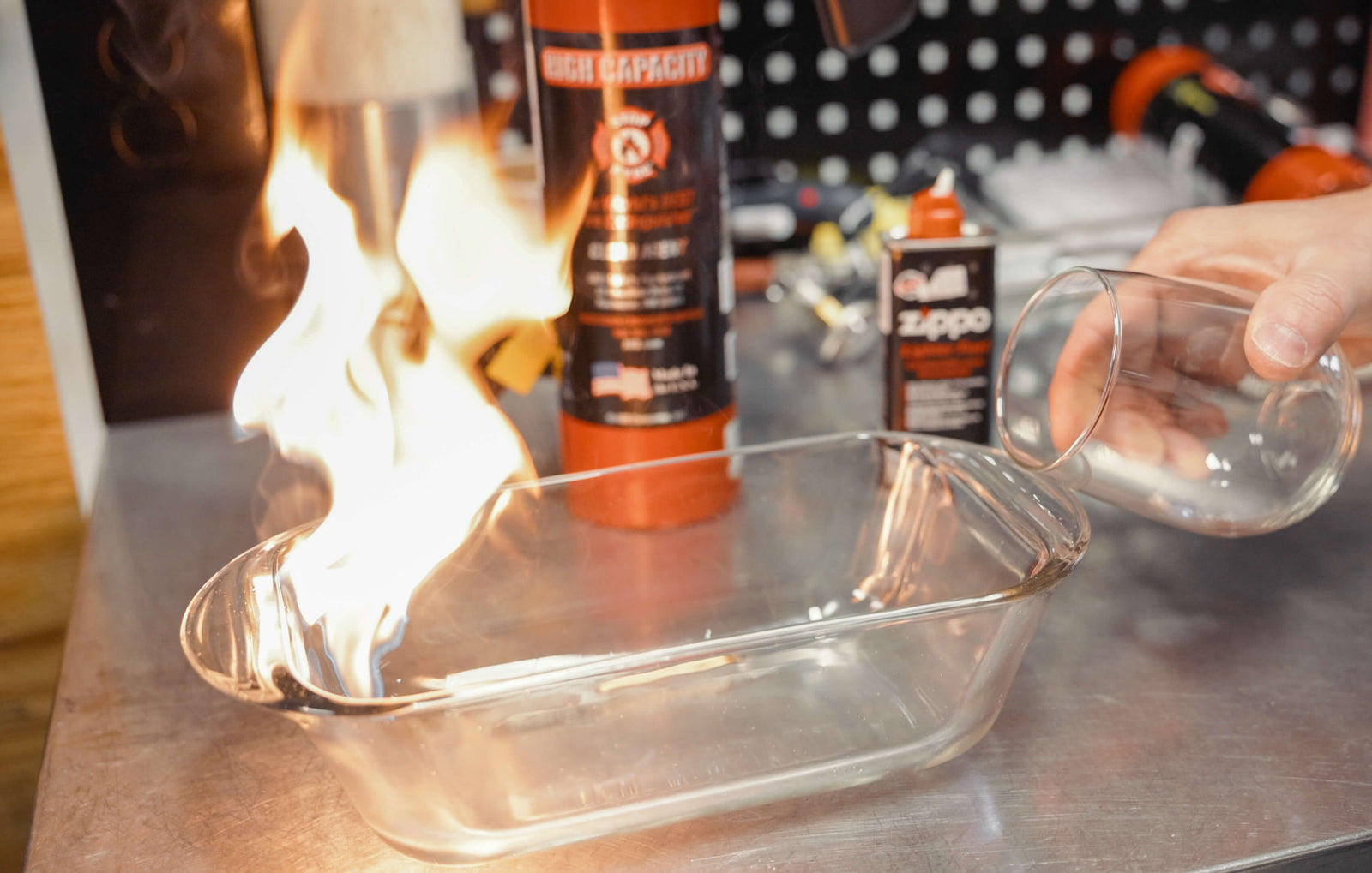 Person pouring stop-fyre into a glass container to put out the fire on a metal surface with Zippo products in the background.